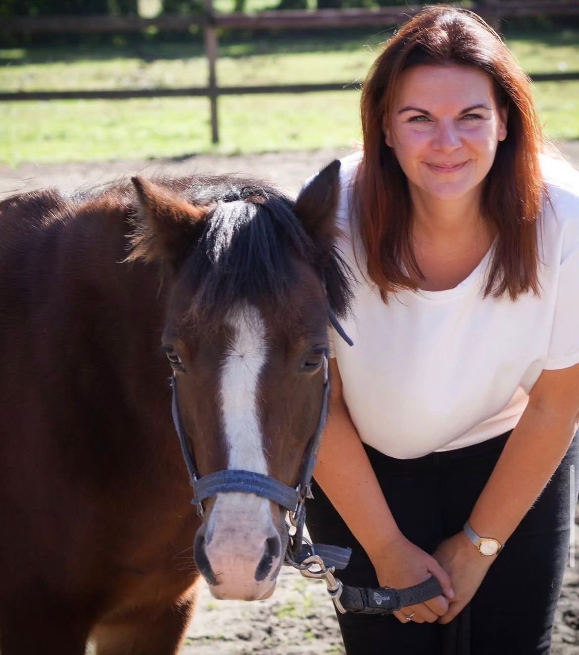 Milou van Laak lachend naast een donkerbruine pony met witte streep op het voorhoofd in de weide